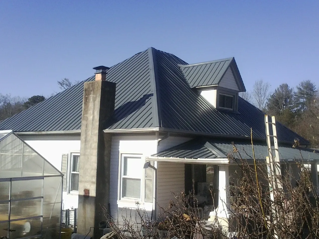 Dark blue standing seam metal roof on a white farmhouse with dormer — Slate & Tile Roof Repair by Roofing Brothers in Cat Spring