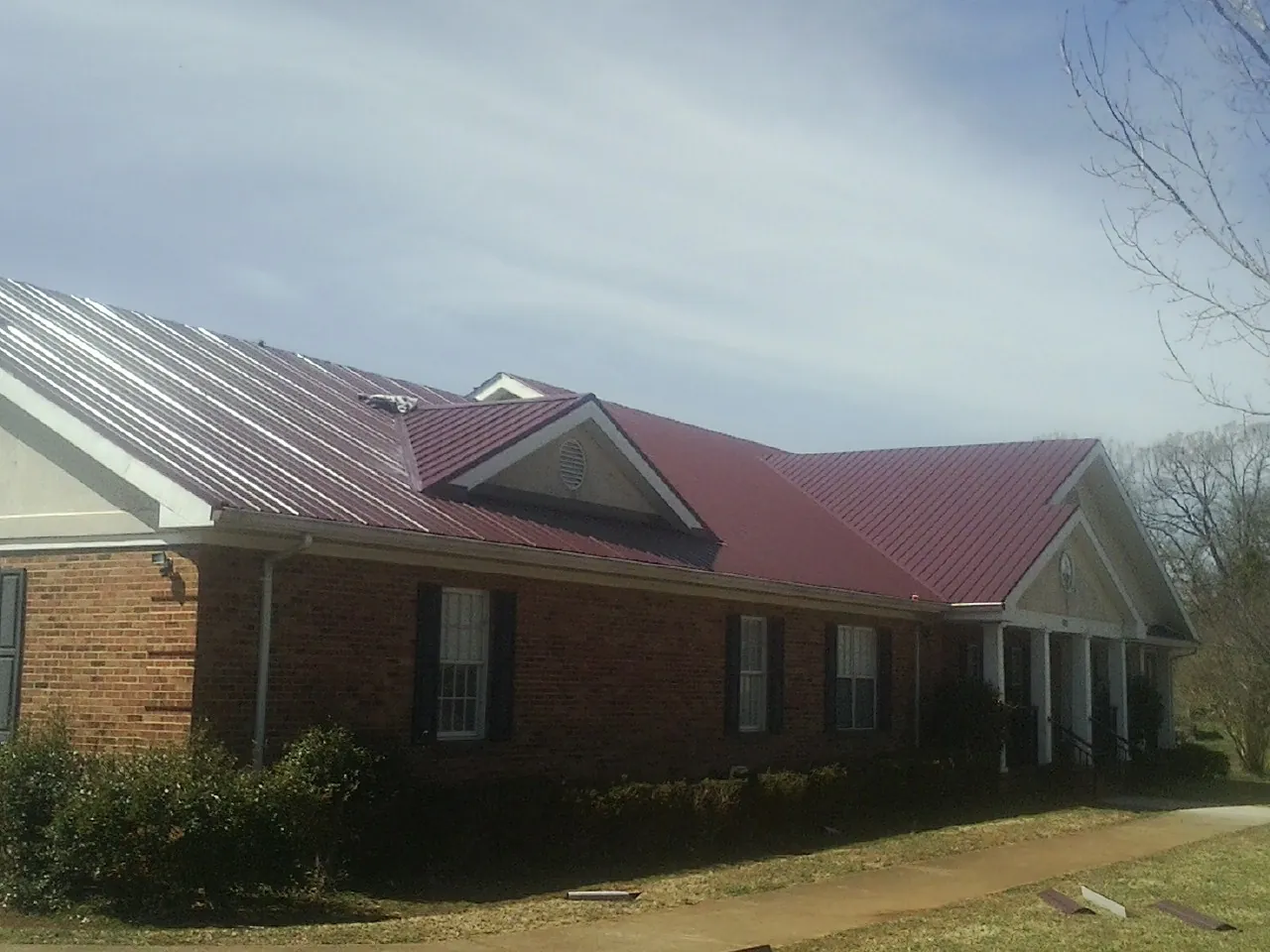 Red metal roof with gabled entries on a long brick building, from a Hail Damage Roof Repair job in Cat Spring