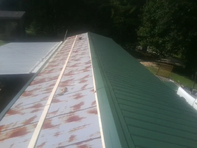 Old rusted panels beside newly installed green metal roofing — Wind Damage Roof Repair by Roofing Brothers in Cat Spring