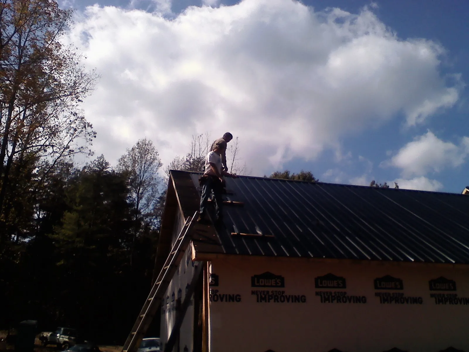 Roofer fastening dark metal panels high against a cloudy sky, from a Roof Inspection job in Cat Spring