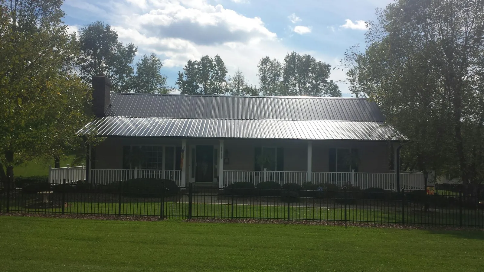 Gray metal roof on a brick ranch with a full width front porch — Gutter Guard Installation work by our crew in Cat Spring