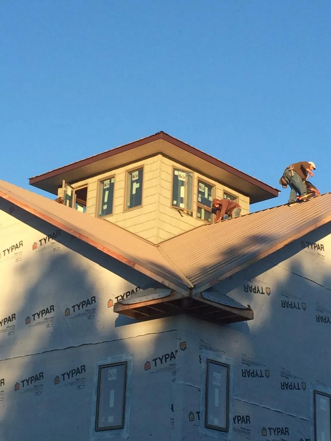 Roofers working around a rooftop cupola on a new metal roof at sunset — Roof Waterproofing in Cat Spring by Roofing Brothers